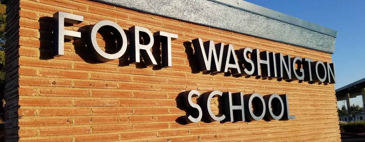 Picture of the Fort Washington school name sign on the brick wall.  Side shot of the sign in front of the school.